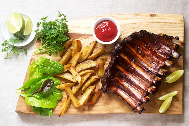 Zelfgemaakte gebakken vleesribbetjes geserveerd met frietjes, kruiden, limoen en ketchup op een houten bord. Rustieke stijl.