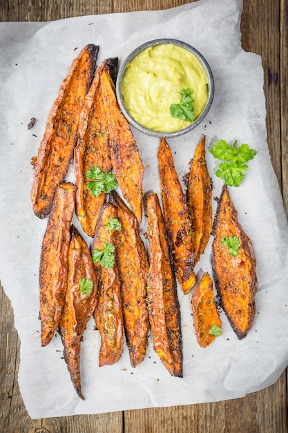 Zelfgemaakte gebakken zoete aardappel met kruiden, zout en peper geserveerd met guacamole saus, op houten ondergrond, bovenaanzicht