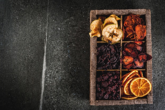 Zelfgemaakte gedroogde bessen en fruit, oogst voor de winter: abrikozen, appels, aardbeien, frambozen, kersen, sinaasappels. In oude houten doos, op zwarte stenen tafelblad weergave