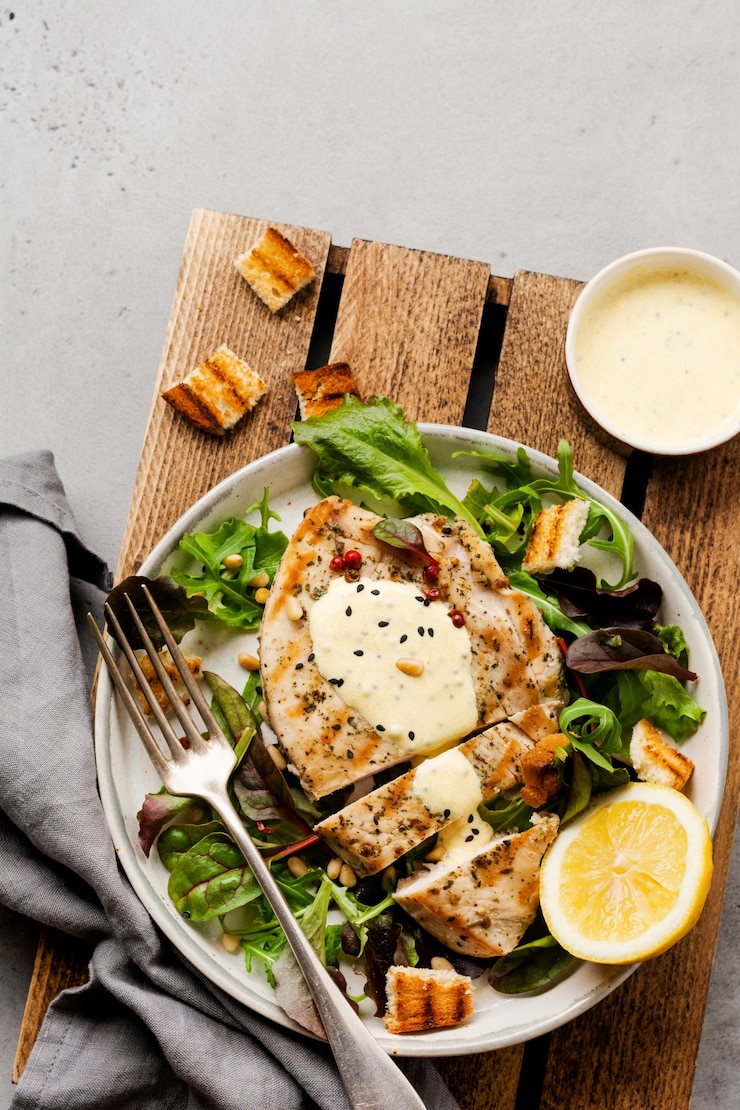 Foto zelfgemaakte gegrilde kalkoensteak met saus, broccoli, rucola en snijbiet in een keramische plaat op een lichte betonnen ondergrond. bovenaanzicht.