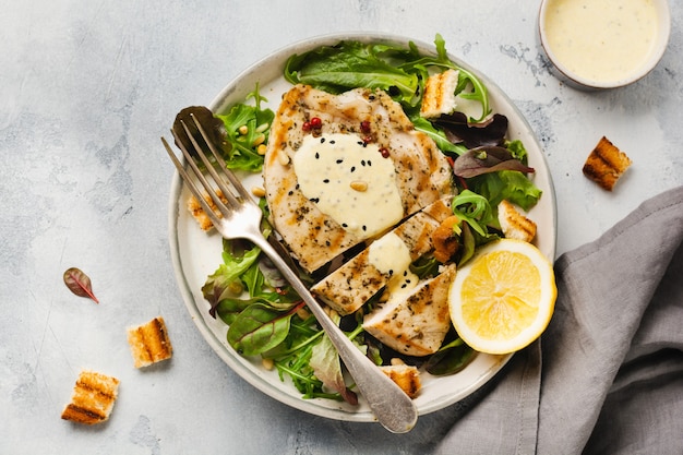 Zelfgemaakte gegrilde kalkoensteak met saus, broccoli, rucola en snijbiet in een keramische plaat op een lichte betonnen ondergrond. Bovenaanzicht.