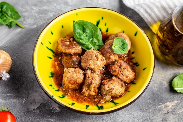 Zelfgemaakte gehaktballetjes met tomatensaus en kruiden geserveerd in gele plaat en een grijs oppervlak