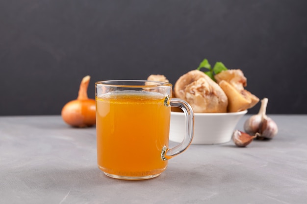 Zelfgemaakte gekookt rundvlees bot bouillon in mok op grijze tafel. Gouden vleesbouillon.