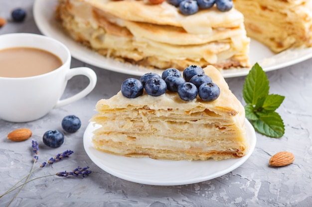 Zelfgemaakte gelaagde Napoleon-cake met melkroom. Versierd met bosbessen, amandelen, walnoten, hazelnoten, mint op een grijze betonnen ondergrond. zijaanzicht, selectieve aandacht.