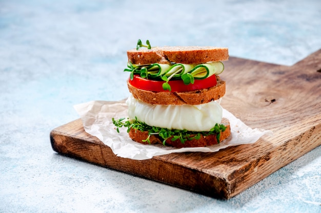 Zelfgemaakte gezonde Sandwich met volkoren brood, gepocheerd ei, komkommer, tomaat en Micro Herbs waterkers salade op houten bord.