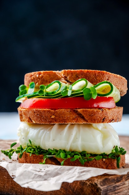 Zelfgemaakte gezonde Sandwich met volkoren brood, gepocheerd ei, komkommer, tomaat en Micro Herbs waterkers salade op houten bord.