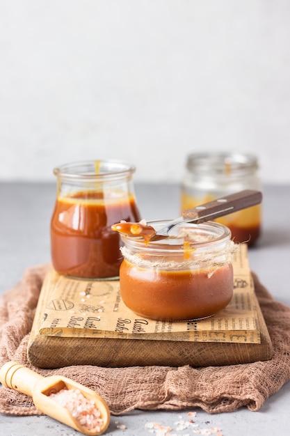 Zelfgemaakte gezouten karamelsaus in glazen potten op houten snijplank.