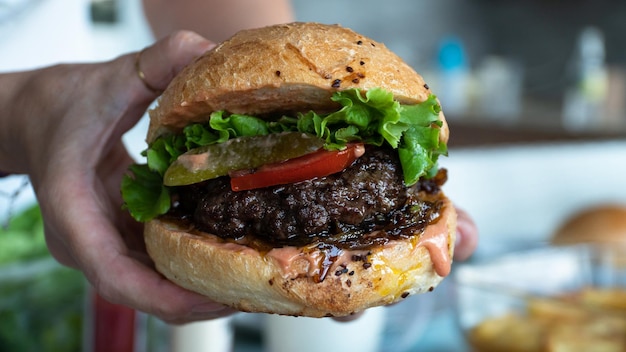 Foto zelfgemaakte hamburger. mannelijke hand met gegrilde zelfgemaakte hamburger. selectieve aandacht inbegrepen.