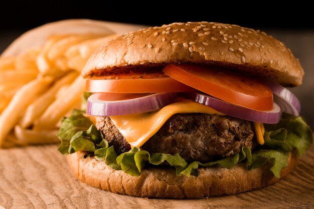 Zelfgemaakte hamburger met rundvlees, ui, tomaat, sla en kaas. Verse hamburger close-up op houten rustieke tafel met frietjes, bier en chips. Cheeseburger.