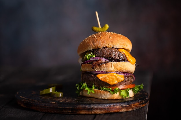 Zelfgemaakte hamburger met twee schnitzels en gesmolten kaas met ui en spek op een houten bord met kopieerruimte