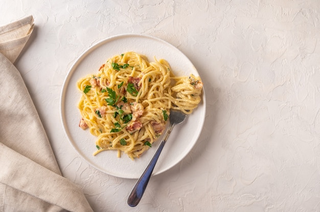 Zelfgemaakte Italiaanse traditionele carbonara pasta met spek, eieren, Parmezaanse kaas op lichte keramische plaat met vork en servet op lichte tafel. Bovenaanzicht