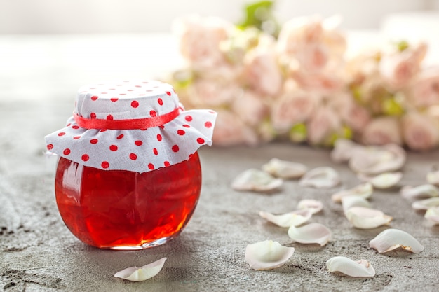 Zelfgemaakte jam van rozenblaadjes op tafel met boeket rozen.