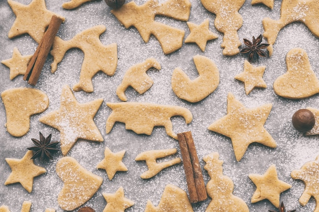 Foto zelfgemaakte kerst- of nieuwjaarskoekjes van verschillende vormen maken op perkamentpapier, bovenaanzicht, plat leggen