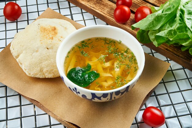 Zelfgemaakte kippenbouillon met handgemaakte pasta en Groenen en focaccio broodje op witte tafel. zelfgemaakte gerechten. Close up bekijken