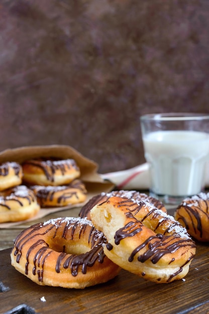 Zelfgemaakte klassieke donuts met chocolade en kokosvlokken en een glas melk op een donkere houten achtergrond. Detailopname.