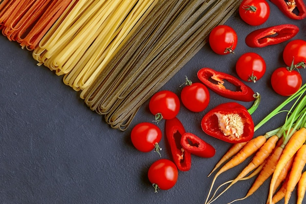 Zelfgemaakte kleurrijke pasta met natuurlijke ingrediënten op een zwarte betonnen tafel noedels met tomaten wortelen paprika