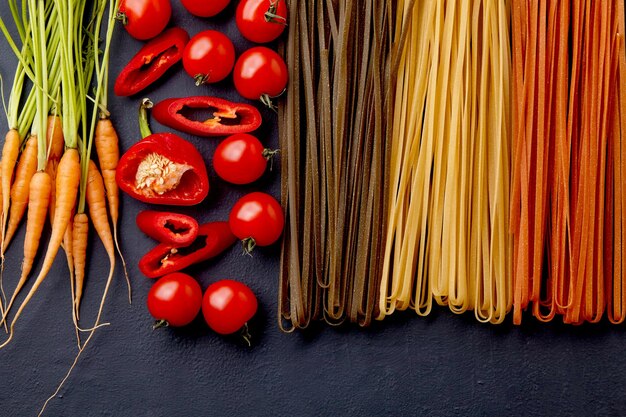 Zelfgemaakte kleurrijke pasta met natuurlijke ingrediënten op een zwarte betonnen tafel Noedels met tomaten wortelen spinazie