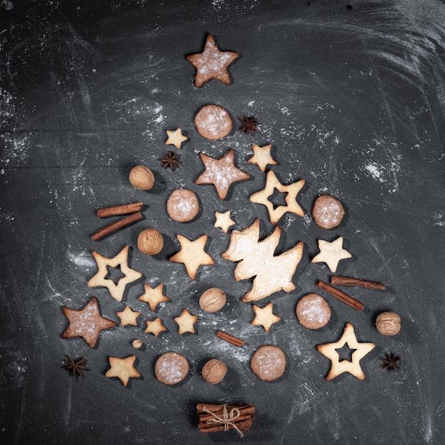 Zelfgemaakte koekjes, kaneel, walnoten, anijs sterren aangelegd als kerstboom op zwart.