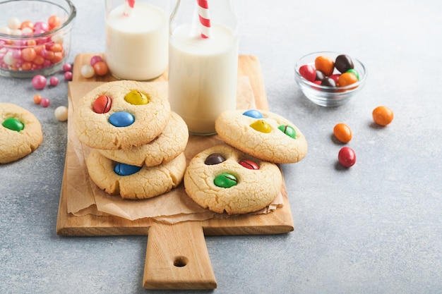 Zelfgemaakte koekjes met kleurrijke chocolade snoepjes en melk Stapel zandkoekkoekjes met multi gekleurde snoep op plaat met fles melk op lichtgrijze achtergrond Babyvoeding concept kopie ruimte