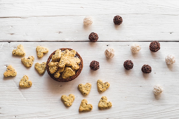 Zelfgemaakte koekjes met kurkuma en lijnzaad in de vorm van hart op witte planken met een mand en klitten van wijnstok. voedsel voor valentijnsdag. uitzicht van boven.