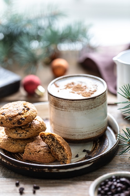 Foto zelfgemaakte koekjes met noten en koffie in een keramische cup op een houten tafel met speelgoed en kerstboomtakken.