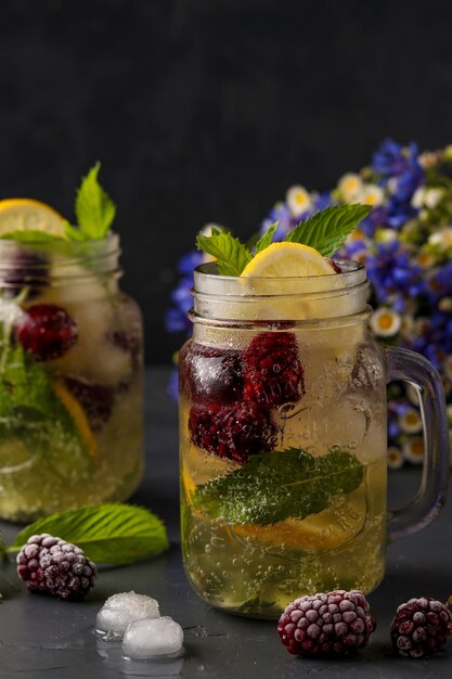 Zelfgemaakte limonade met citroen, bramen en munt in glas tegen een donkere achtergrond