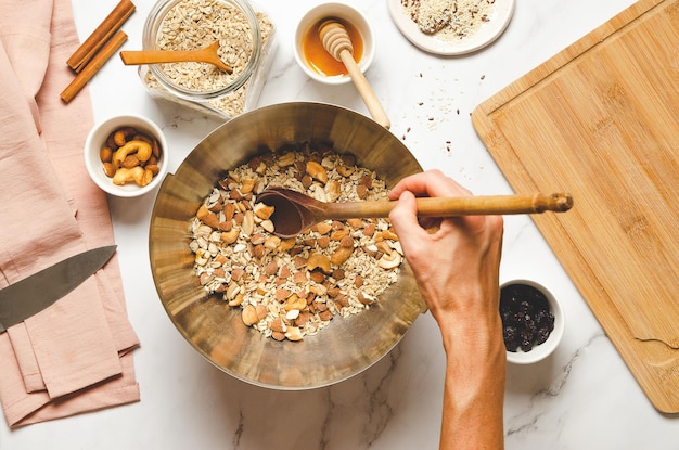 Zelfgemaakte muesli koken Bovenaanzicht van een vrouw die havermout en noten mengt in een kom met een houten lepel