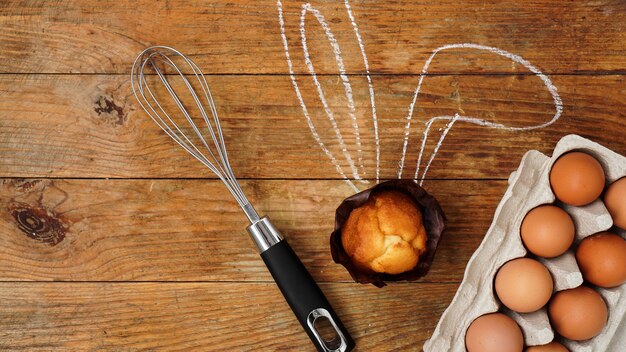 Zelfgemaakte muffin met geschilderde konijnenoren. muffin, klop en eieren op een houten oppervlak