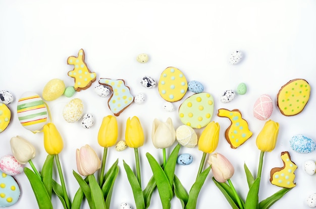 Zelfgemaakte ontbijtkoekkoekjes van Pasen met suikerglazuur, versierde eieren en tulpen op een witte achtergrond