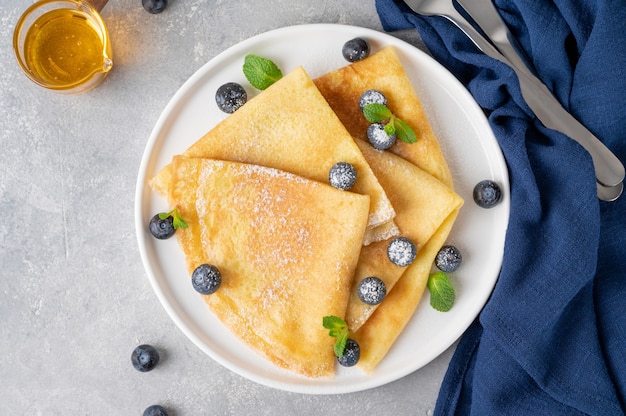 Zelfgemaakte pannenkoeken geserveerd met verse bosbessen en poedersuiker op een witte plaat op een grijze betonnen achtergrond. Voedsel voor Maslenitsa. Kopieer ruimte.