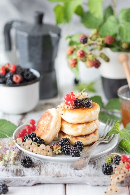 Zelfgemaakte pannenkoeken met bessen, de bramen, de honing op de plaat, een tak van een BlackBerry-wekker op witte houten achtergrond