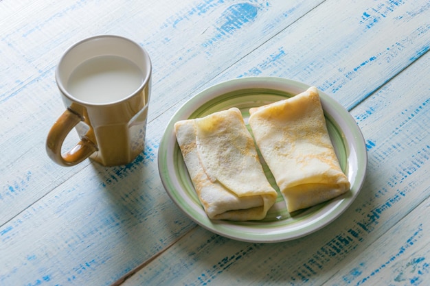 Zelfgemaakte pannenkoeken met een vulling en een kopje melk op een houten ondergrond