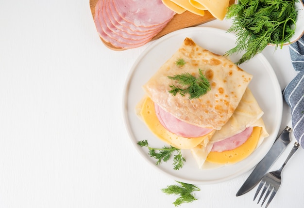 Zelfgemaakte pannenkoeken met ham en kaas op een witte ondergrond, Maslenitsa, bovenaanzicht