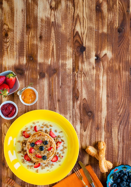 Zelfgemaakte pannenkoeken met verse bessen, aardbeien, bosbessen en ahornsiroop op een houten oppervlak.