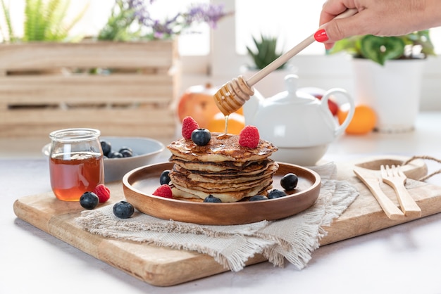 Zelfgemaakte pannenkoeken met verse bosbessen, frambozen en honing. Vrouwelijke hand gieten honing