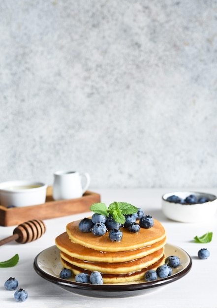 Zelfgemaakte pannenkoeken op een witte plaat met honing en bosbessen voor het ontbijt. Goedemorgen!