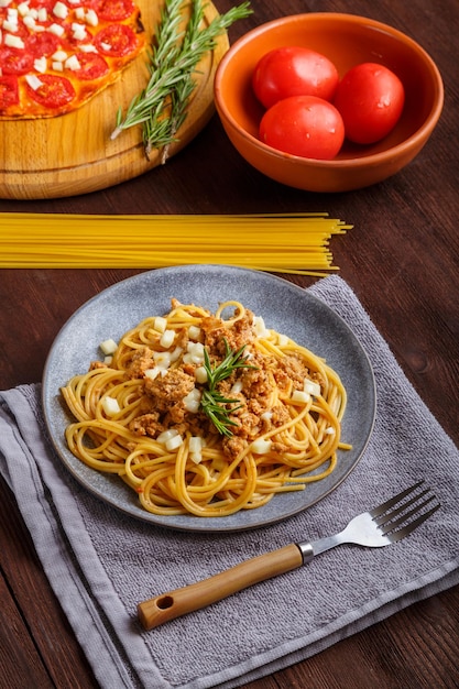 Foto zelfgemaakte pasta bolognese op een bord en pizza met tomaten op een houten tafel