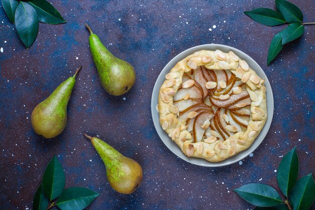 Zelfgemaakte peer galette taart met amandel bladeren en verse rijpe groene peren