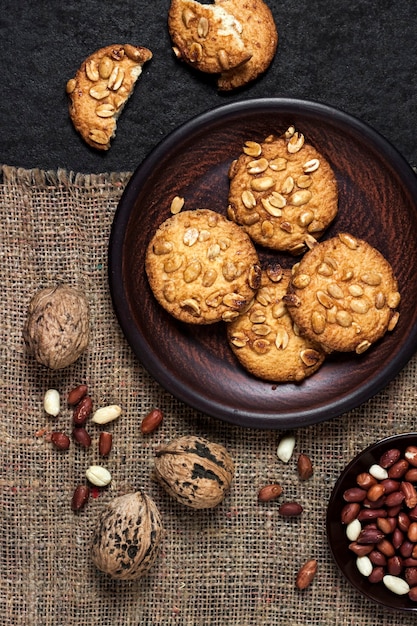 Zelfgemaakte pindakoekjes op een bruine plaat met ruwe pinda's op achtergrond. Rustiek eten. Plat lag, bovenaanzicht