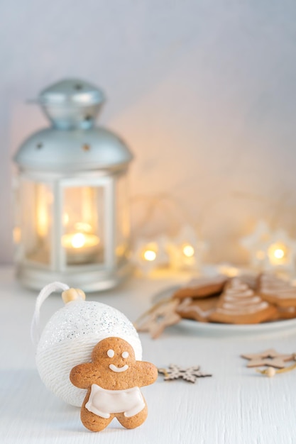 Zelfgemaakte pittige gingerbread man koekje op witte houten tafel met guirlande lichten en kerstbal