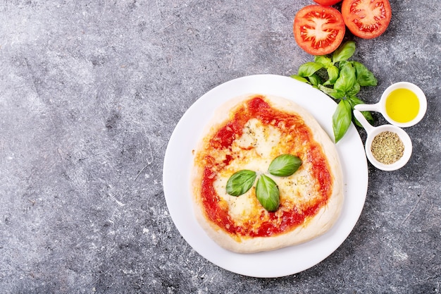 Zelfgemaakte pizza margherita met mozzerala kaas geserveerd met verse basilicum, kruiden oregano en tomaten over blauwe textuur oppervlak. Bovenaanzicht, plat gelegd. Kopieer ruimte
