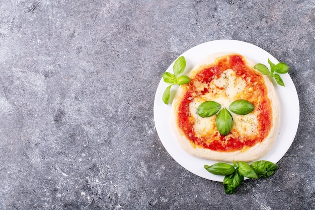 Zelfgemaakte pizza margherita met mozzerala kaas geserveerd met verse basilicum, kruiden oregano en tomaten over blauwe textuur oppervlak. Bovenaanzicht, plat gelegd.