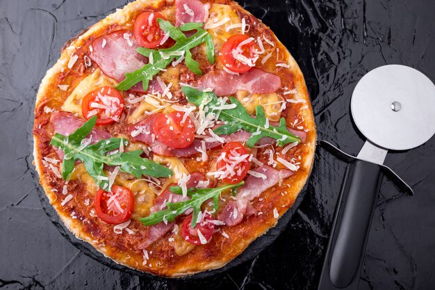 Zelfgemaakte pizza met prosciutto, tomaat, rucola op zwarte leisteen bord. Bovenaanzicht