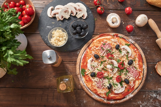 Zelfgemaakte Pizza op een houten bord, met tomaten en salami, champignons, Italiaanse stijl op oude houten tafel, bovenaanzicht