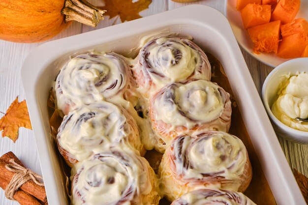 Foto zelfgemaakte pompoen kaneelbroodjes met roomkaas in een ovenschaal, plat gelegd, bovenaanzicht. seizoensgebonden herfst zelfgemaakt gebak - kaneel voor ontbijt of vakantie.