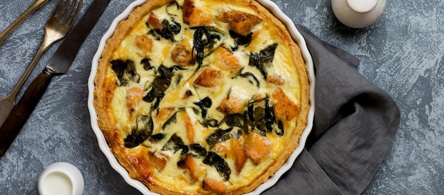 Zelfgemaakte quiche taart met rode vis en spinazie op lichte houten achtergrond. vintage-stijl. bovenaanzicht.