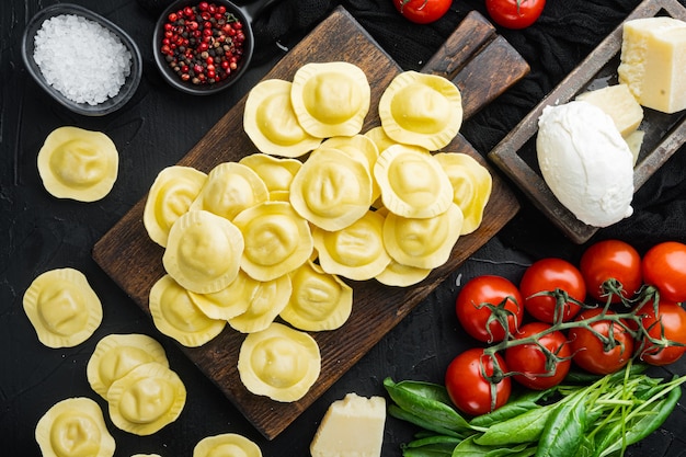 Zelfgemaakte Ravioli met mozzarella kaas en basilicum set, op houten snijplank, op zwarte tafel, bovenaanzicht plat lag