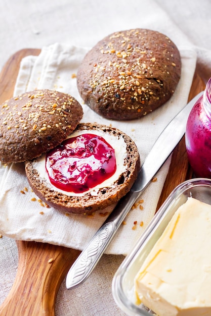 Zelfgemaakte roggebroodjes met lijnzaad, sesam en witte maanzaad geserveerd met boter en jostabessenjam op een houten bord