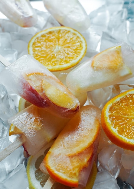 Zelfgemaakte sinaasappel- en perzikijslollys met ijs en citrusschijfjes op lichte achtergrond Zomervoedselconcept lekker fruitijs