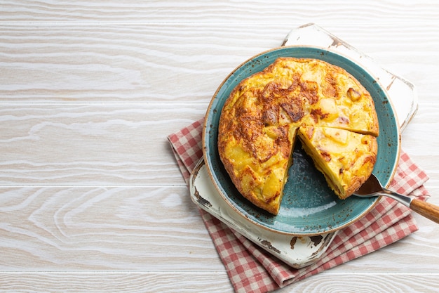 Zelfgemaakte Spaanse tortilla met één plak gesneden - omelet met aardappelen op plaat op witte houten rustieke achtergrond bovenaanzicht. Traditioneel gerecht van Spanje Tortilla de patatas voor lunch of snack, kopieer ruimte